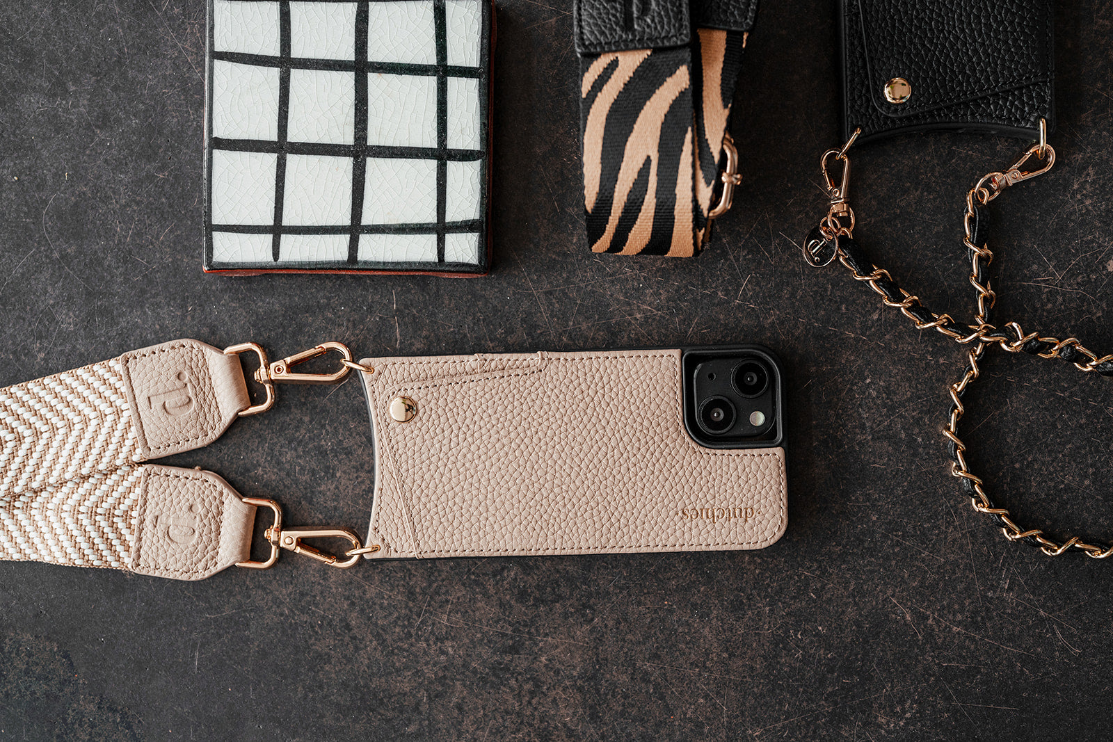 Stylish iPhone 15 PRO MAX Case with a strap, surrounded by various trendy accessories.
