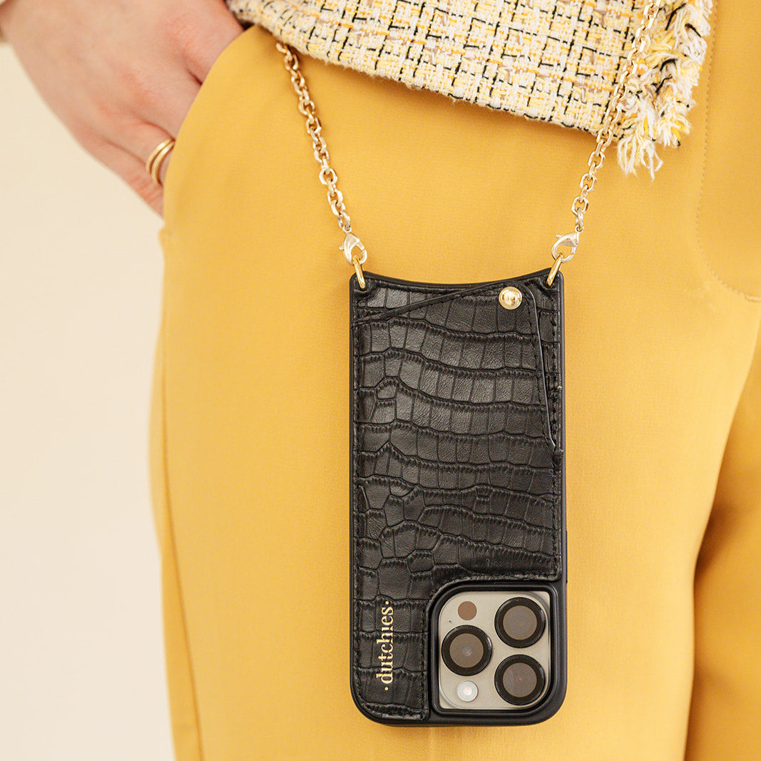 A chic Noir Gold phone case with a chain, styled elegantly with a yellow outfit, showcasing modern fashion.