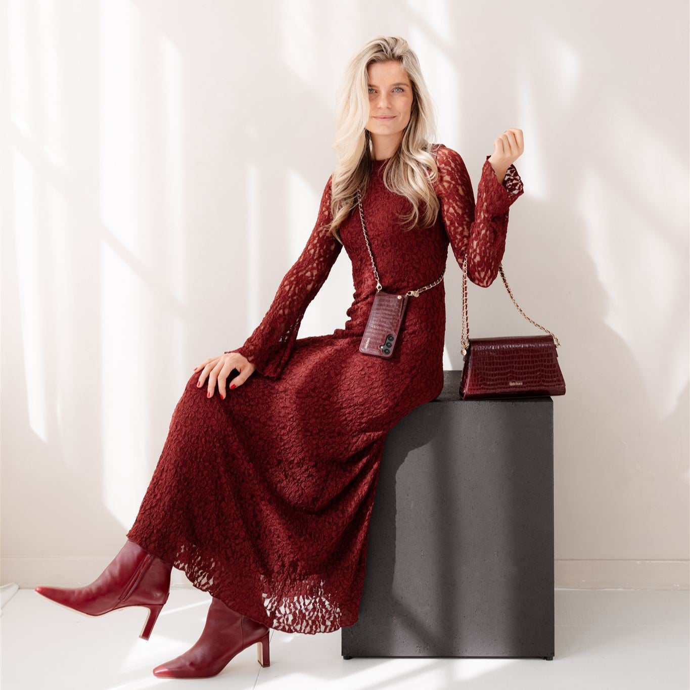 Woman in a burgundy dress and boots, posing stylishly with a burgundy handbag, showcasing the Burgundy collection.