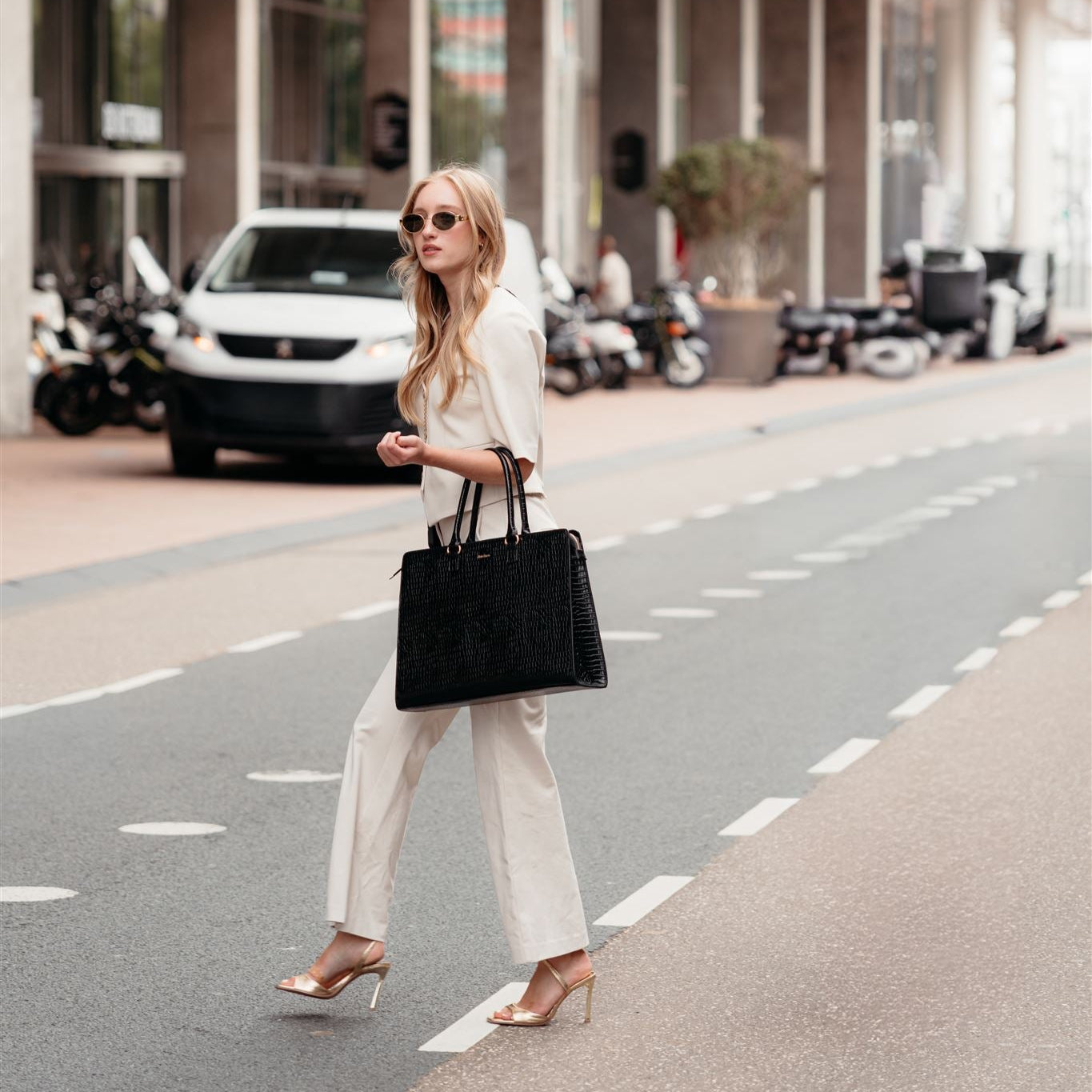 Stylish woman in Office Wear crossing the street with a black tote bag and sunglasses.