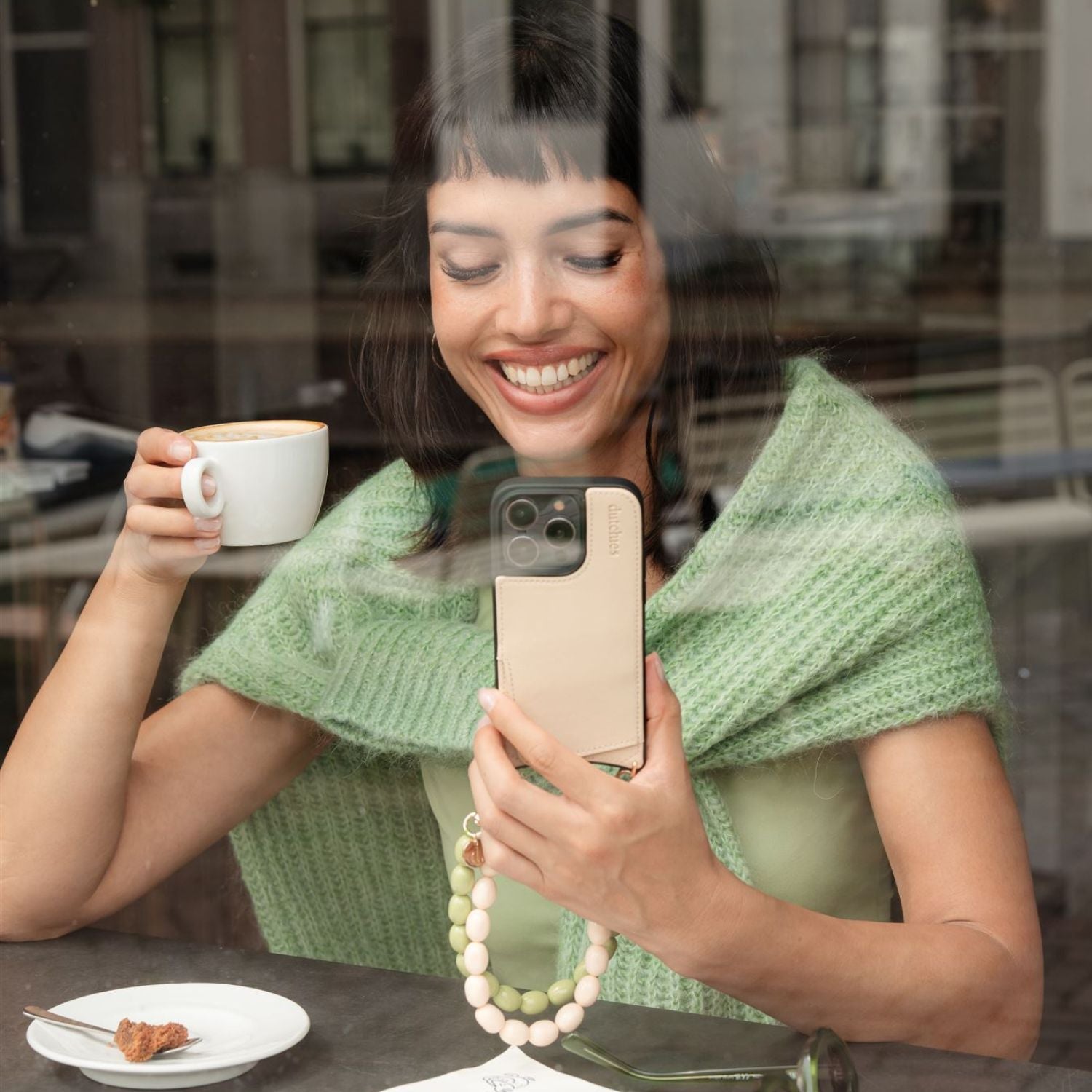 Smiling woman enjoying coffee and showcasing her style in a cozy setting for Our Bestsellers collection.