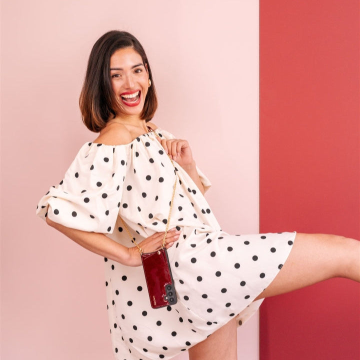 Woman in a polka dot dress happily showcasing Phone Chain | Spanish | Gloss Red against a colorful backdrop.