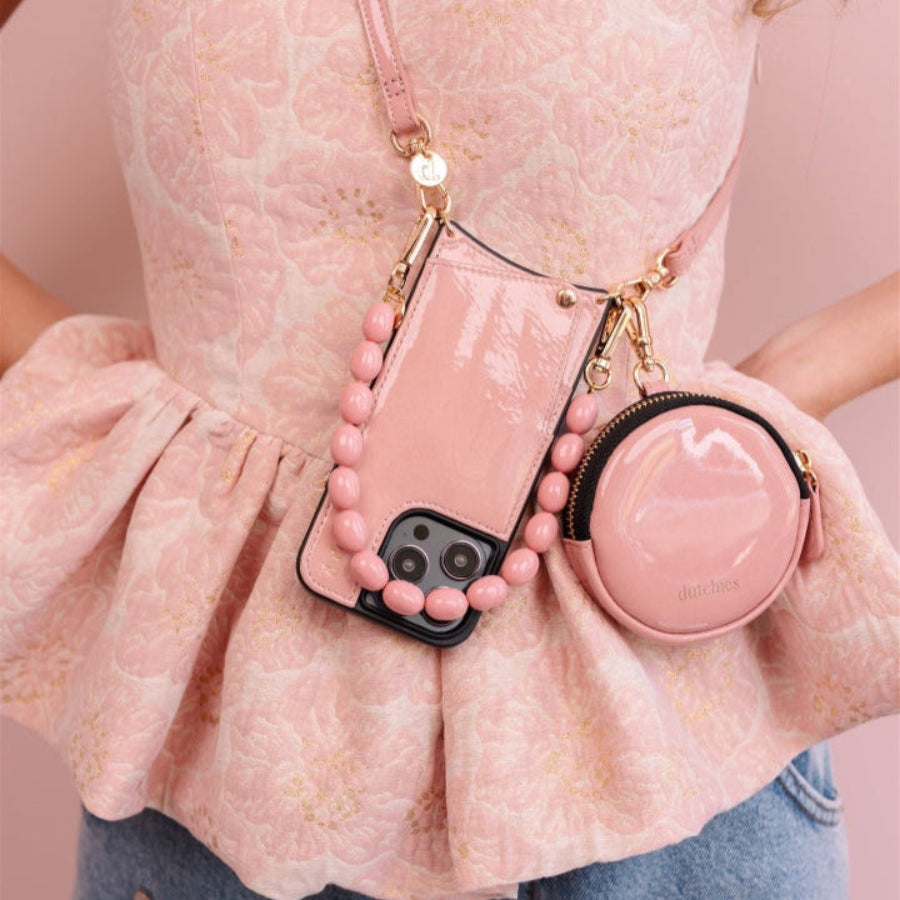A person wearing a pink floral dress with a gloss pink iPhone case and a matching round purse attached to a gold chain.