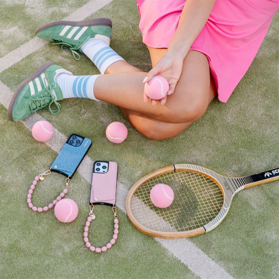 Stylish pink phone charms and tennis balls on a court, with a player in a pink dress and green sneakers.