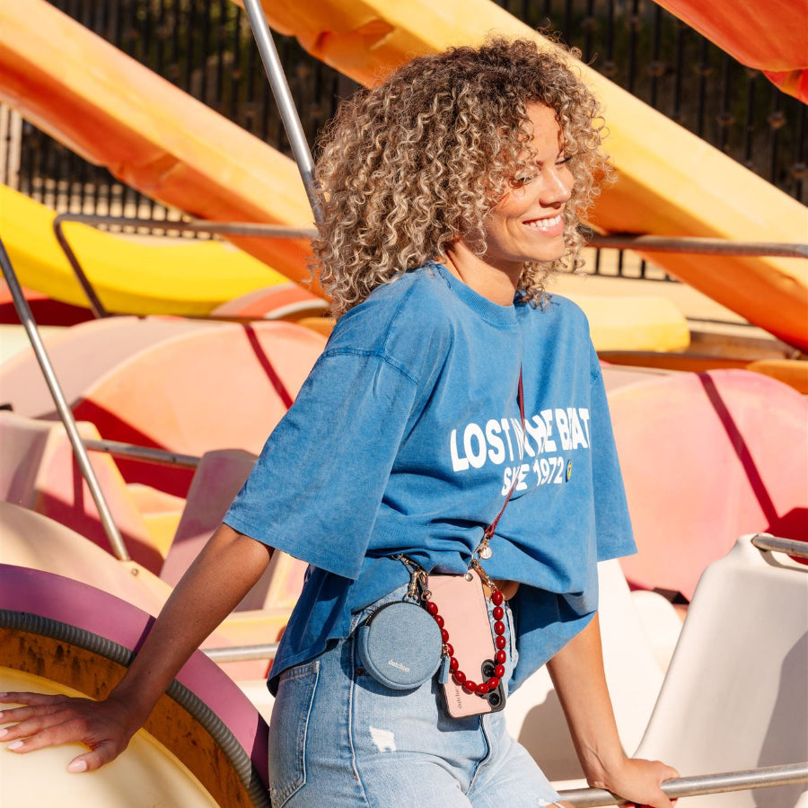 A woman wearing a blue shirt and beaded phone charm, smiling at a fun amusement park setting.