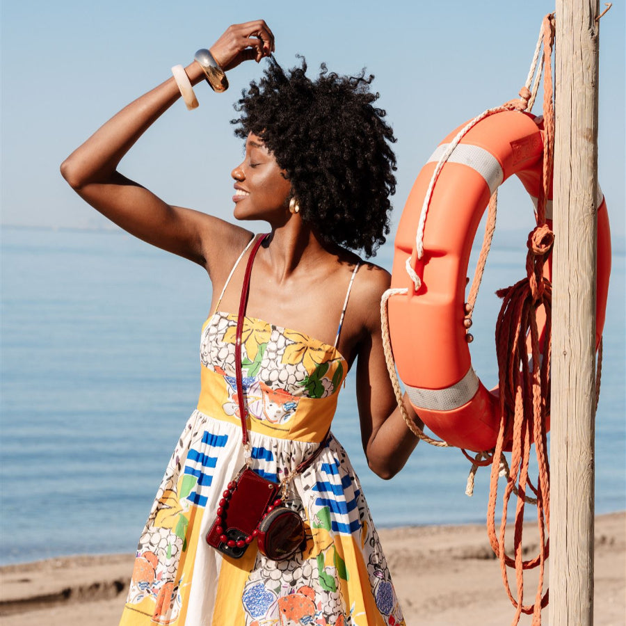 Woman in colorful dress enjoying a sunny beach day with a beaded phone charm.
