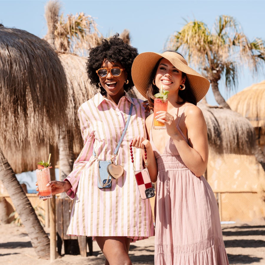 Two friends enjoying summer cocktails at a beach, showcasing vibrant beaded phone charms.