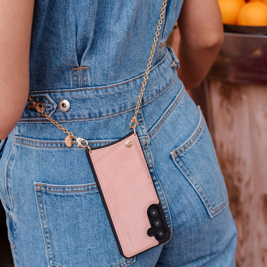 Person wearing a pink phone case with a chain on blue jeans, standing in front of fruit display.