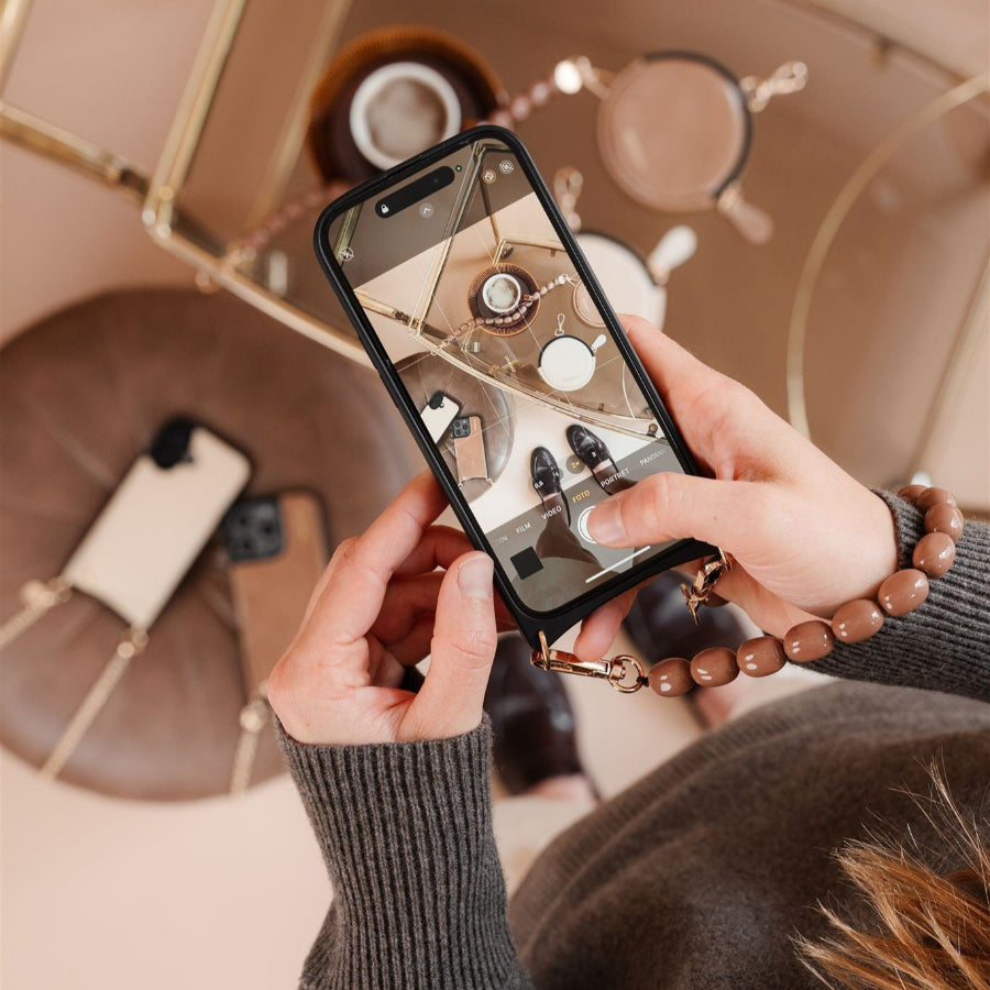 Close-up of a hand holding an iPhone Case | Vanilla with a strap, showcasing a stylish flat lay.