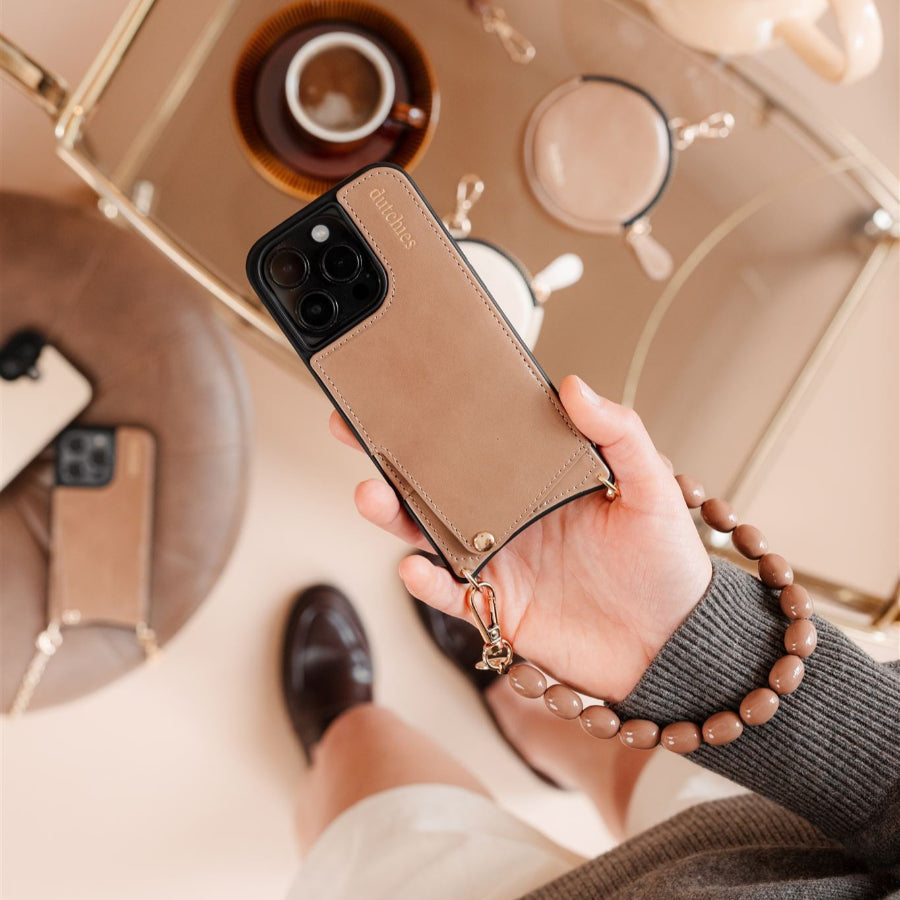 Hand holding a stylish phone case with strap, showcasing a modern design and elegant accessories on a table.