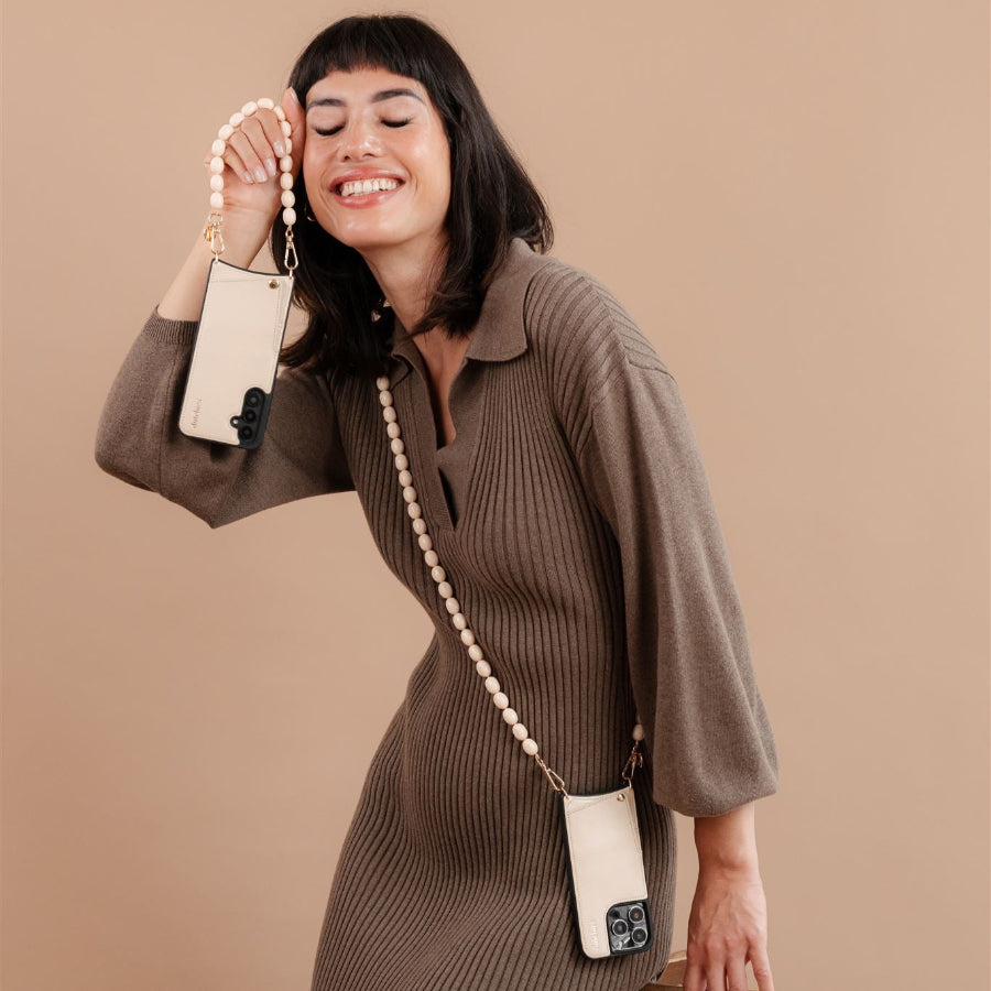 Woman wearing a beaded phone chain Gwen, showcasing an elegant style with a beige phone case and a joyful expression.
