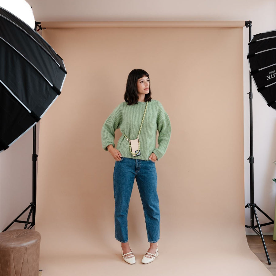 Model wearing a green sweater and jeans, showcasing a stylish phone charm in a photo studio setting.