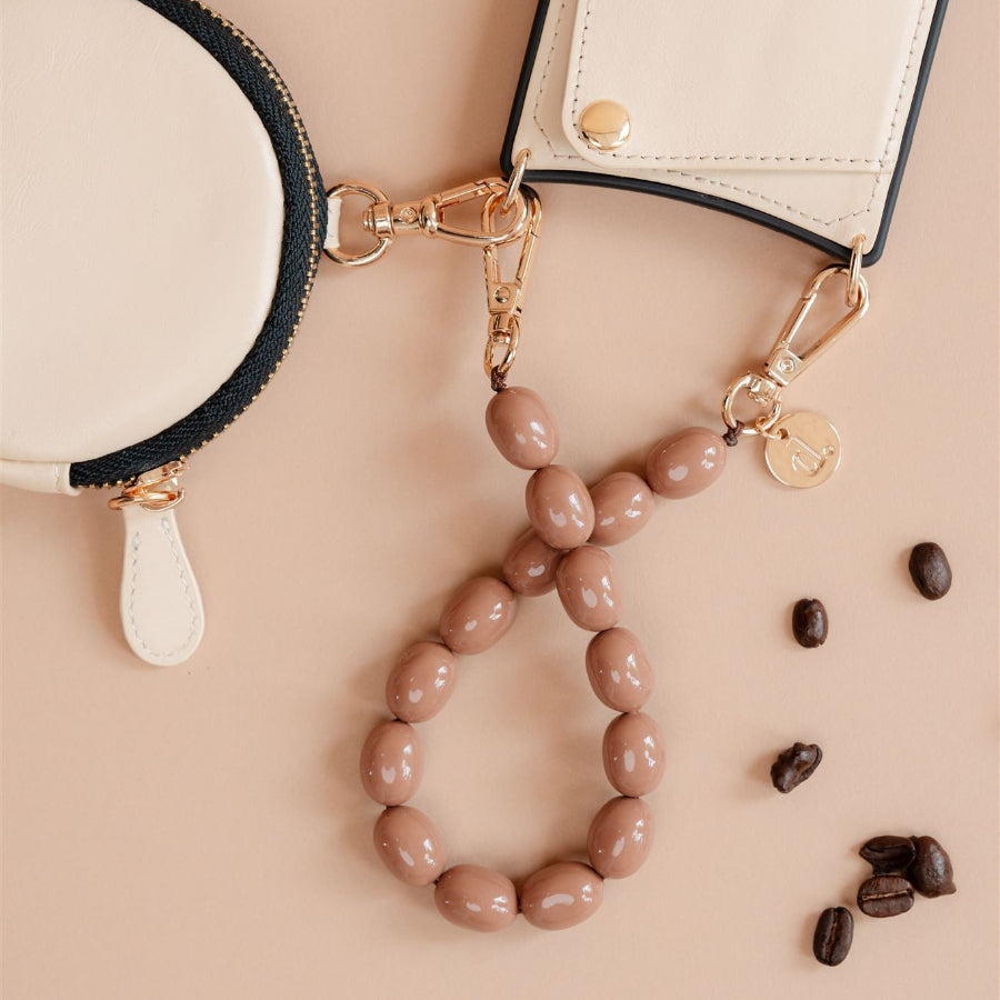 Close-up of the Rachel phone charm strap with round beads, alongside a cream pouch and coffee beans.