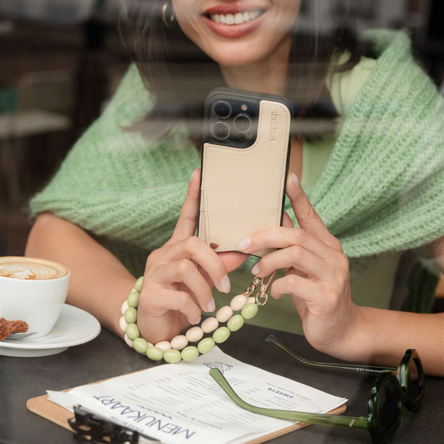 Woman holding a beaded phone charm with a custom phone case at a cafe, showcasing the stylish accessory.