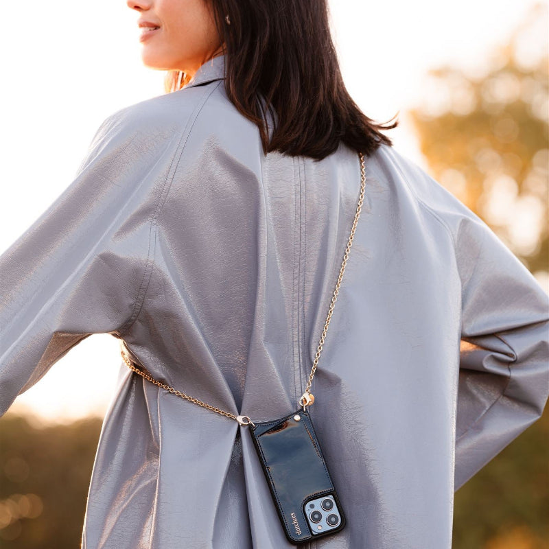 Person wearing a light gray coat with a phone case on a chain over their shoulder, blurred outdoor background