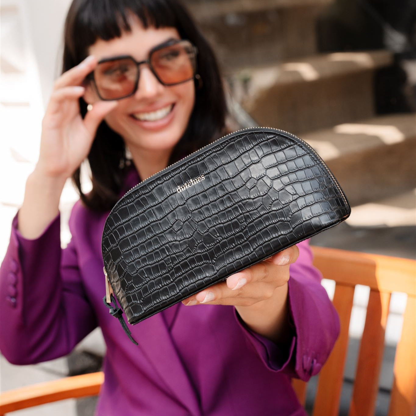 Stylish black leather pouch with crocodile texture, held by a smiling woman in glasses, perfect for work essentials.