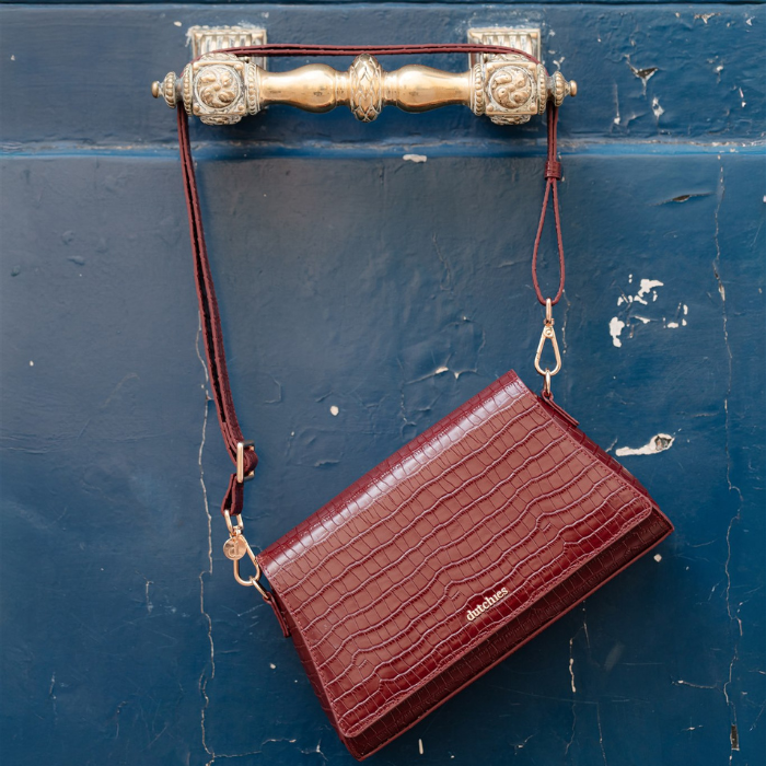 Sophie Crossbody Bag | Burgundy hanging on a gold door handle, featuring a luxurious crocodile texture.