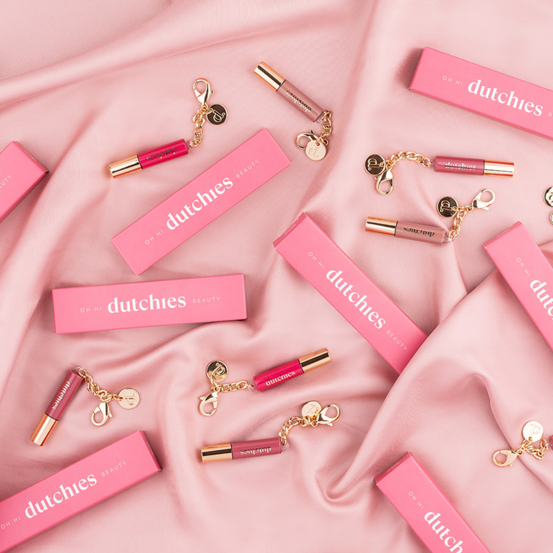 Colorful Lipgloss | Keychain products displayed with chic packaging on soft pink fabric.