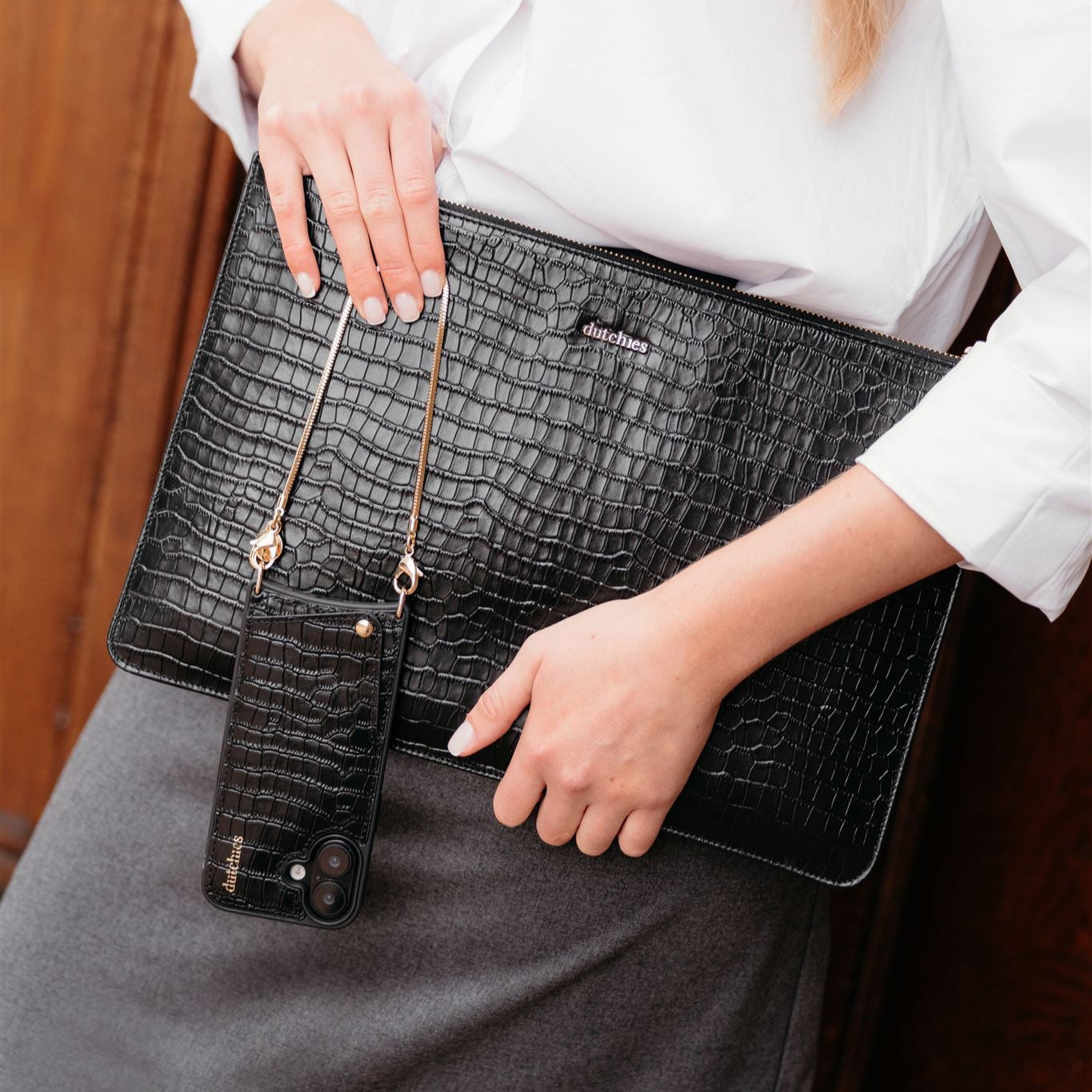 Stylish black croc-embossed laptop sleeve held by a woman with a matching phone case, perfect for chic tech protection.