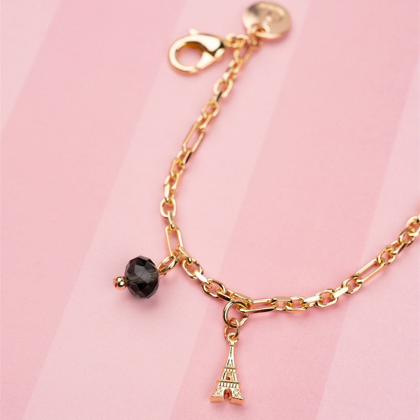 Gold phone charm with a black bead and Eiffel Tower charm on a pink background