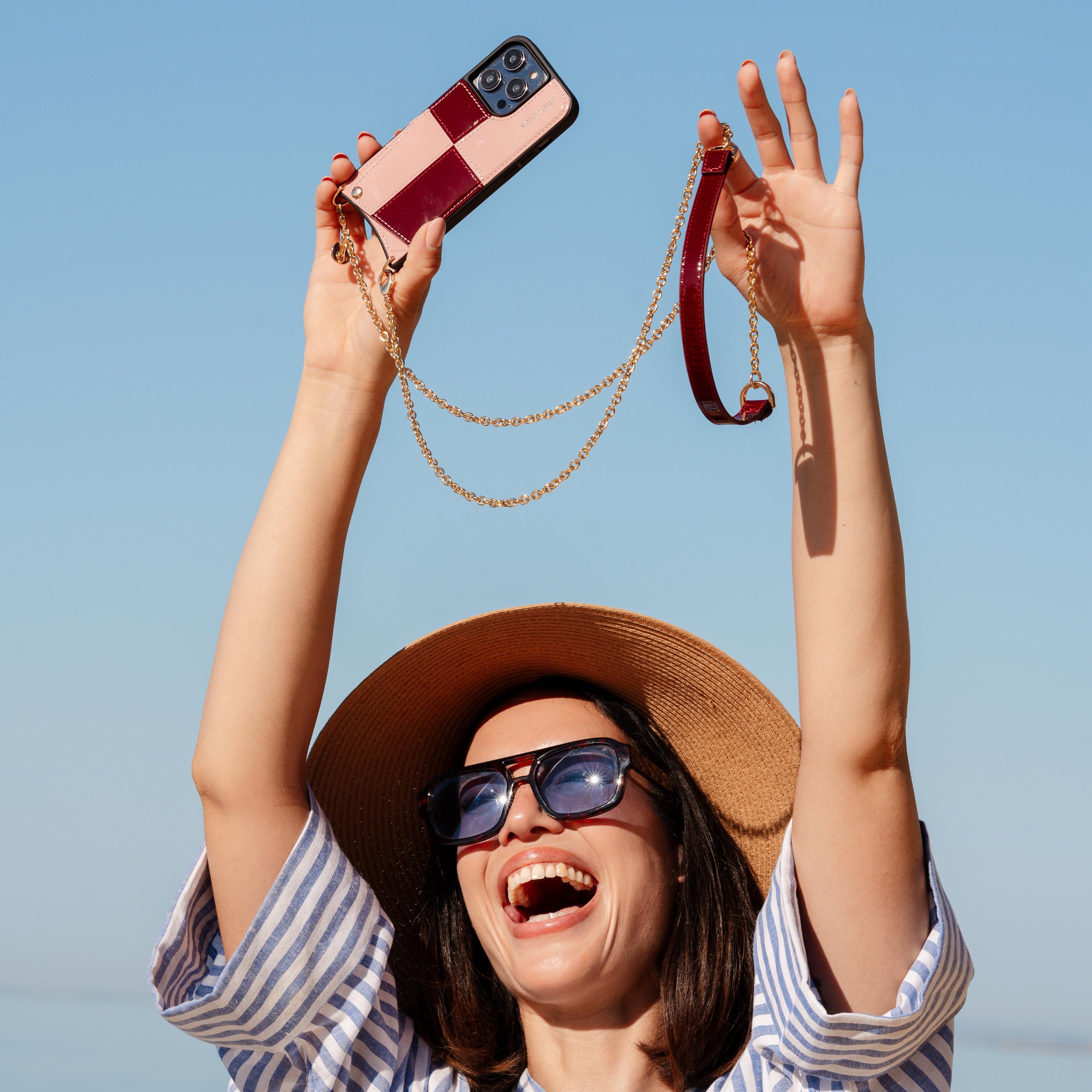 Woman in a straw hat and sunglasses holding up a phone with a case against a clear blue sky.