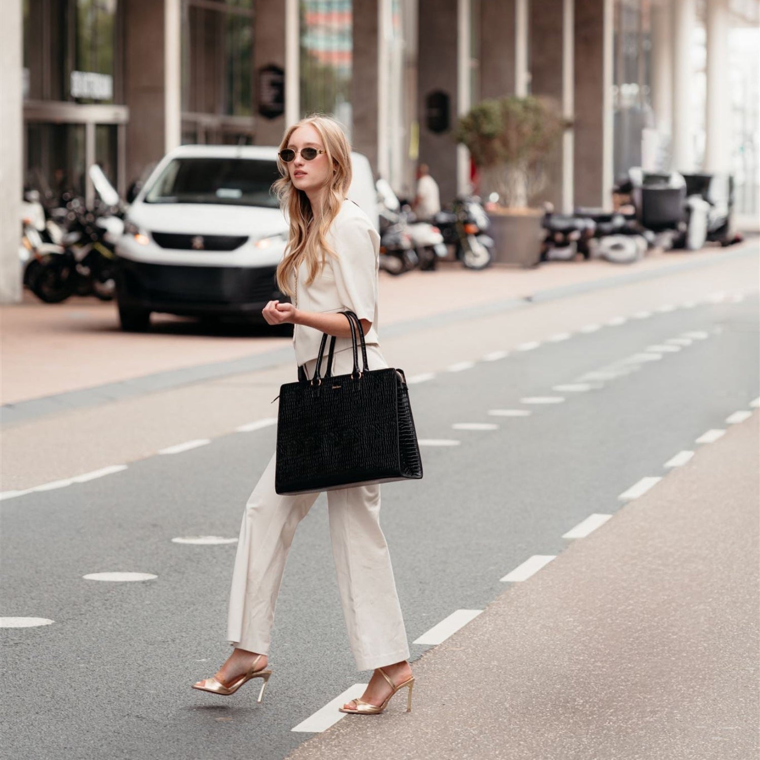 Fashionable woman in stylish beige outfit carrying a chic black laptop bag while walking on the street.