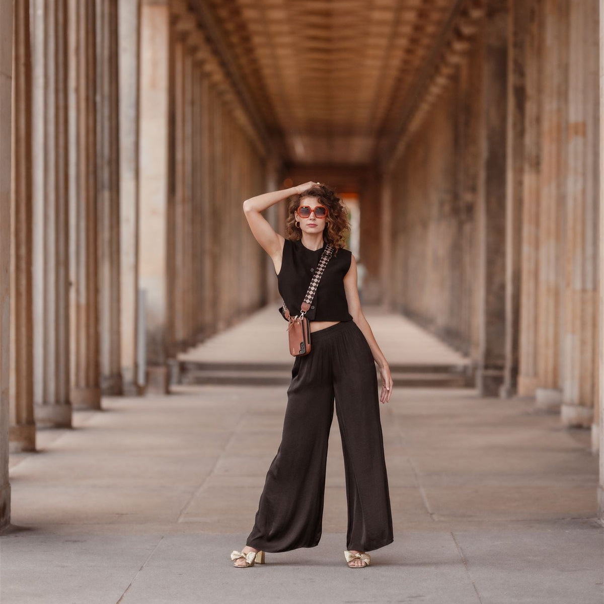 Woman posing confidently in a black outfit with a Phone Bag ROSE | Brown in a colonnade.