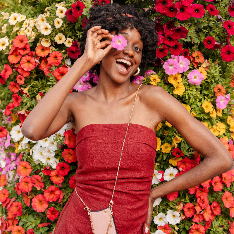 Femme joyeuse en robe rouge posant avec une fleur devant un décor floral coloré.