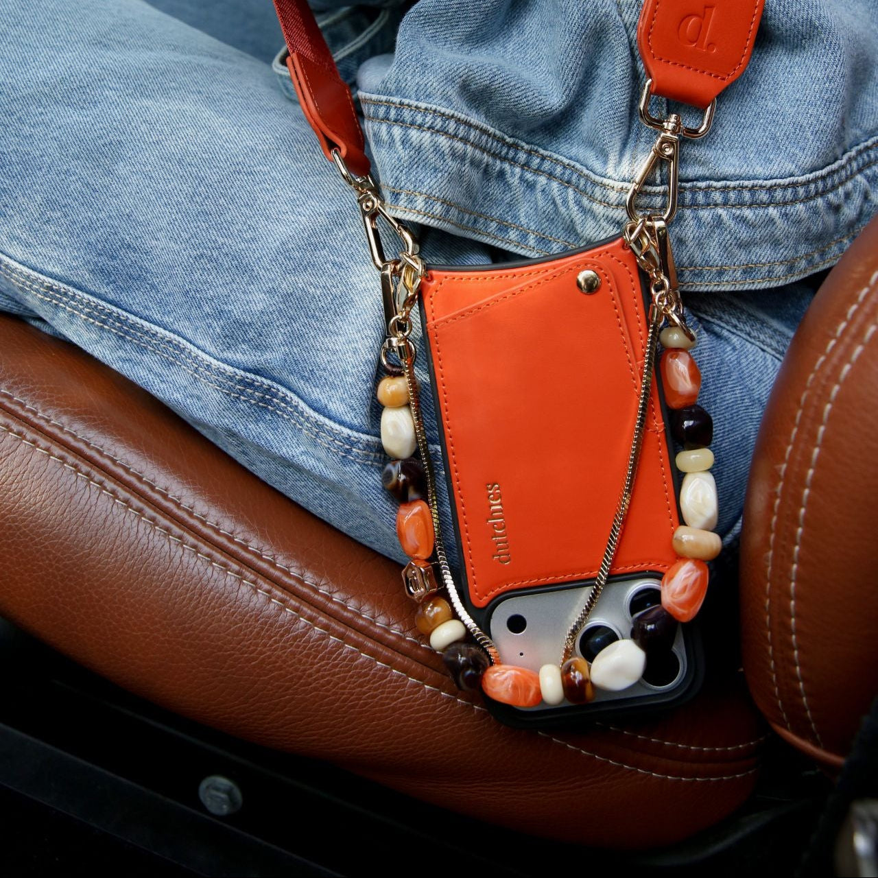 Phone Charm | Beaded | Sonia attached to an orange wallet, resting on a brown leather seat, showcasing creativity and elegance.