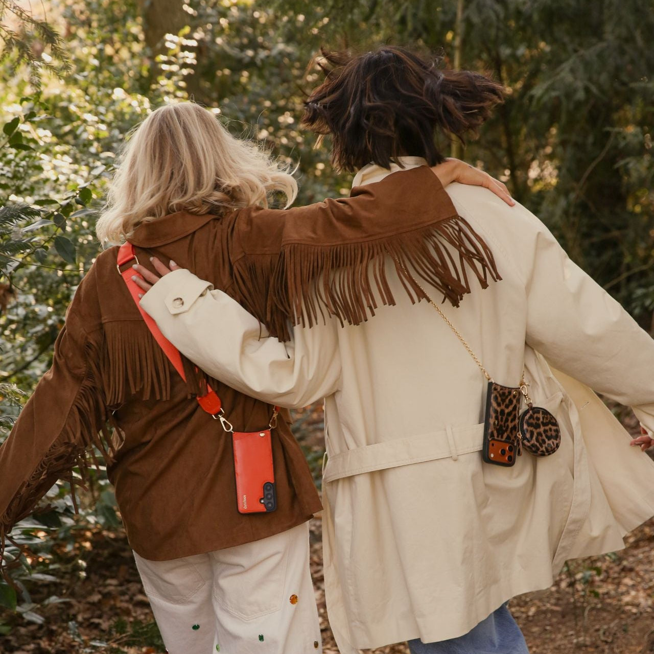 Two friends wearing fringe jackets, showcasing the Mini Phone Bag Emma | Leopard in a forest setting.