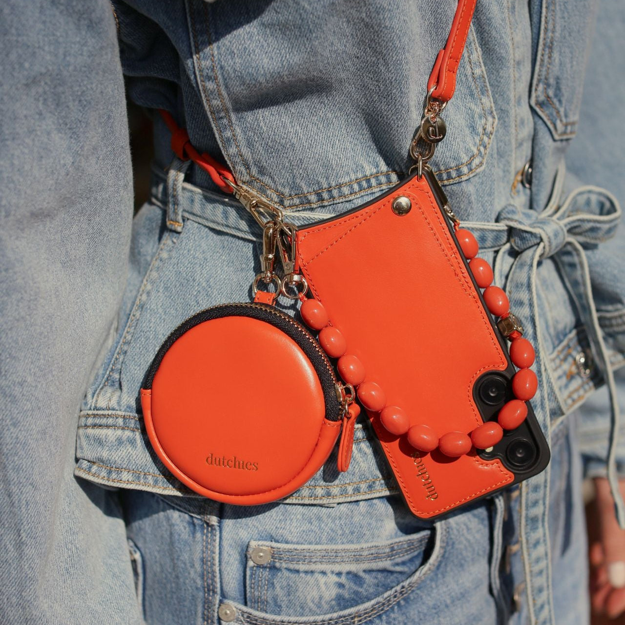 Mini Phone Bag Emma | Orange stylishly clipped onto a denim jacket, featuring a round pouch and other accessories.