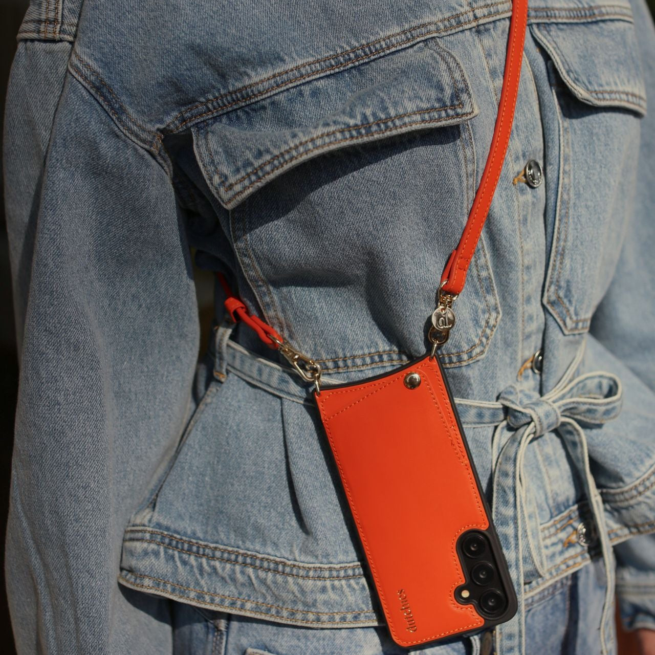 Phone strap | Slimline | Orange attached to a stylish outfit, showcasing trendy and practical design.