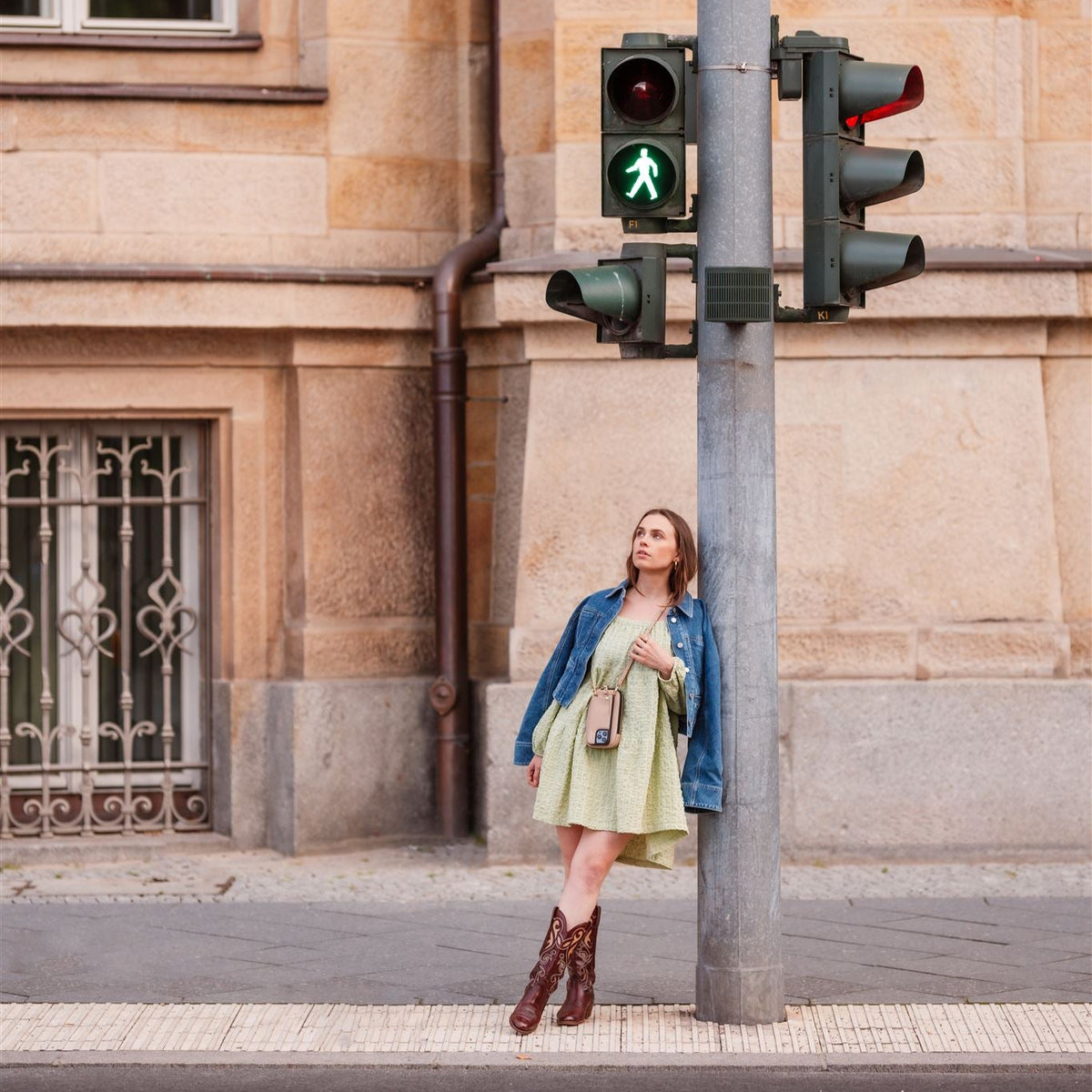 A stylish woman in a denim jacket and dress stands by a traffic light, showcasing a chic Phone Bag ROSE | Beige.