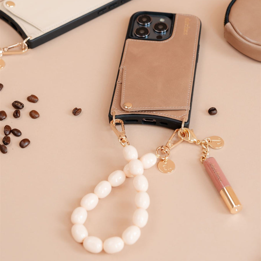 Beaded phone charm attached to a smartphone case, featuring a stylish design with cream beads and a lipstick tube.