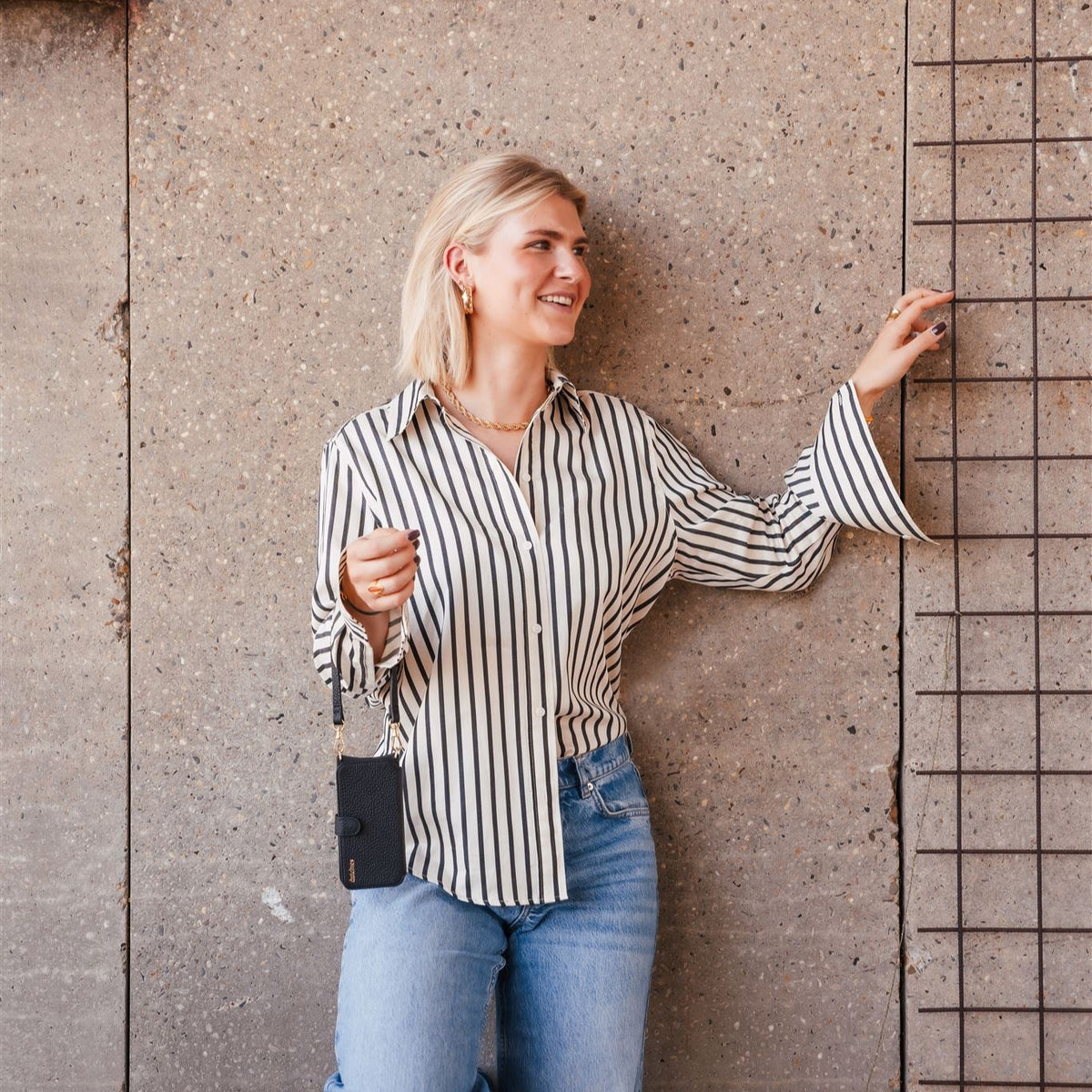 Woman wearing a striped shirt and jeans, showcasing the Phone Charm | Slimline | Black hanging from her hand.