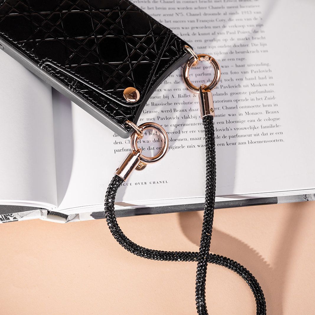 Black glitter Phone Charm | Glitter | Coco attached to a stylish case, resting on an open book.