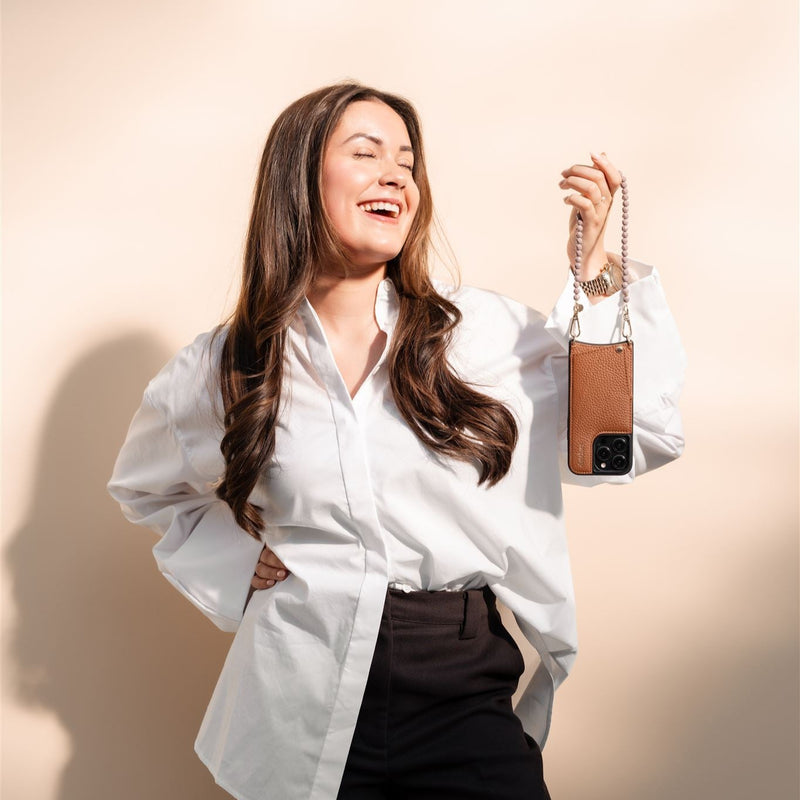 Woman smiling wearing a white shirt, holding a Phone Charm | Beaded | Aletta with a phone attached.
