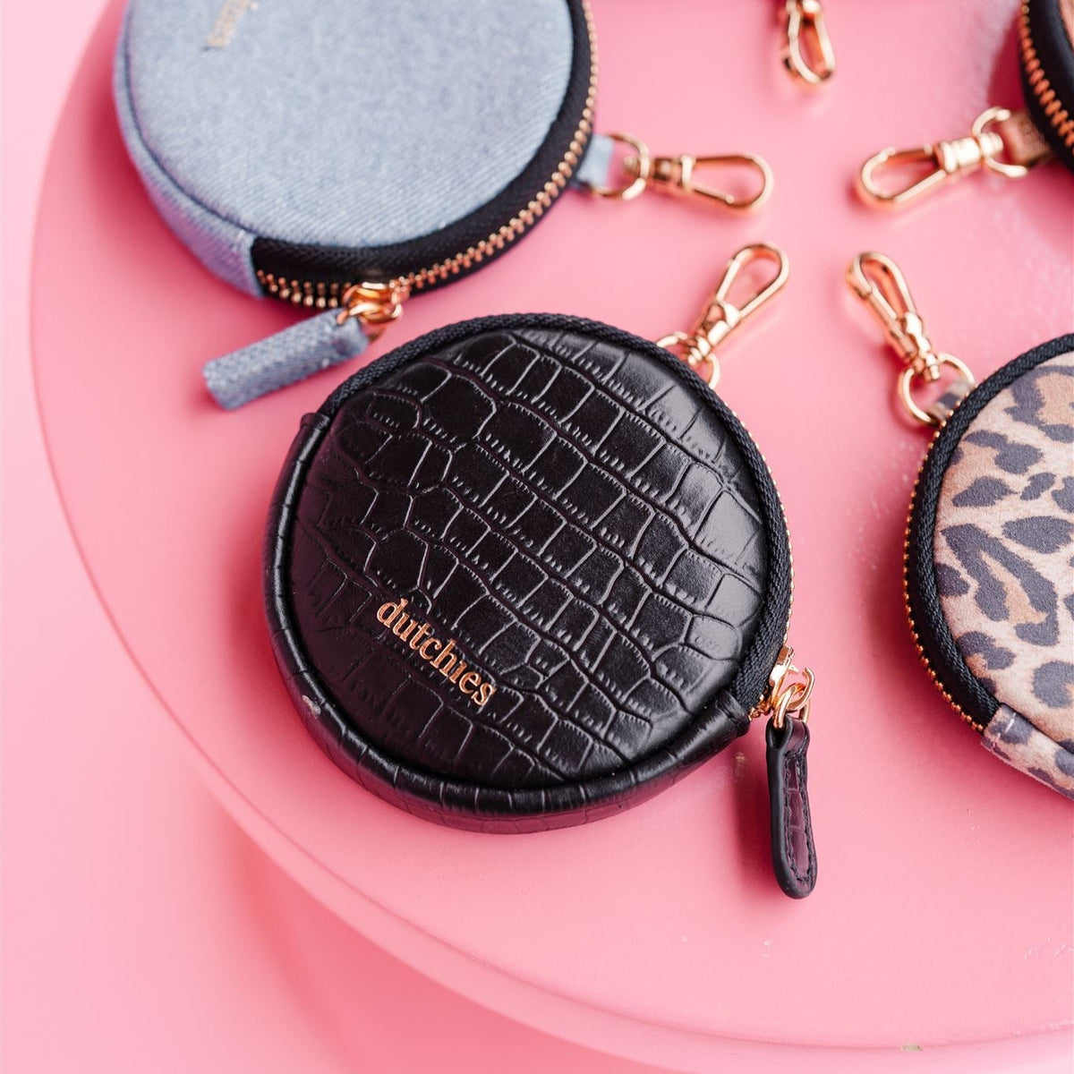 Mini Phone Bag Emma | Noir | Gold on pink table, round pouch with gold accents and leather texture.