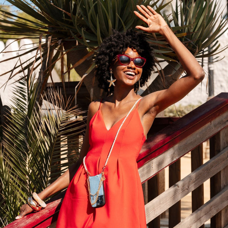 A woman in a vibrant red dress enjoys the sun while wearing trendy sunglasses and a stylish phone charm.