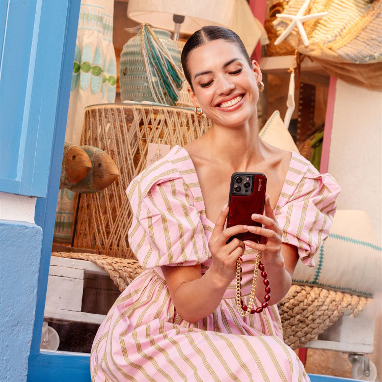 Woman in pink striped dress holding Phone Charm | Gold | French while sitting in a cozy shop setting.