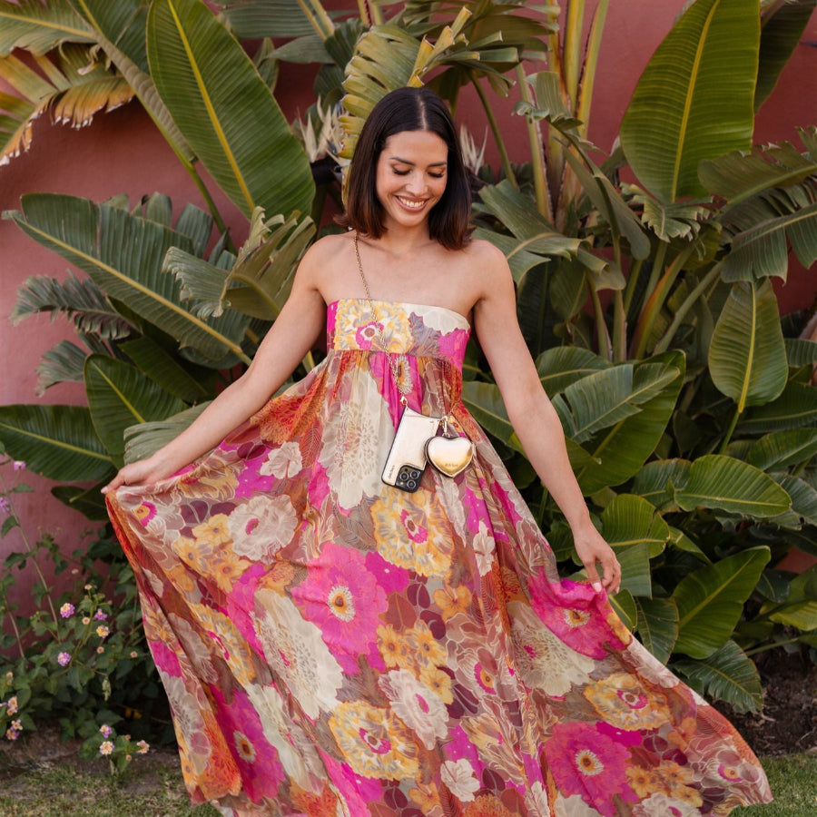 Phone Chain | Spanish | Goldy on stylish woman in floral dress with purse, against tropical backdrop.
