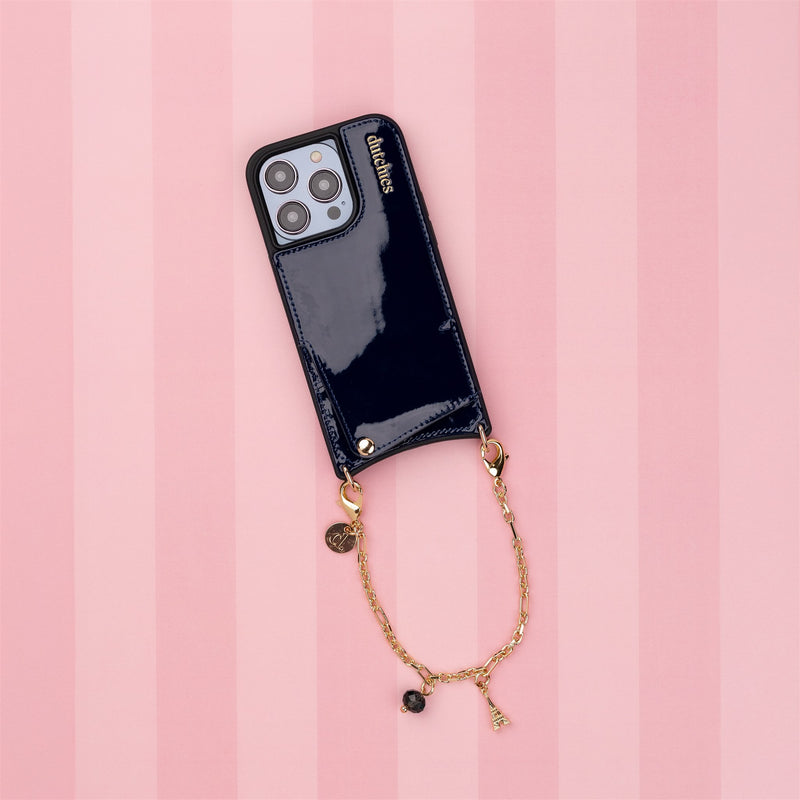 Phone Charm | Gold | Dutch Bandolier attached to a navy phone case on a pink striped background.