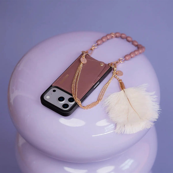 iPhone Case | Mauve on a round purple surface with a strap and fluffy charm, showcasing elegant design.