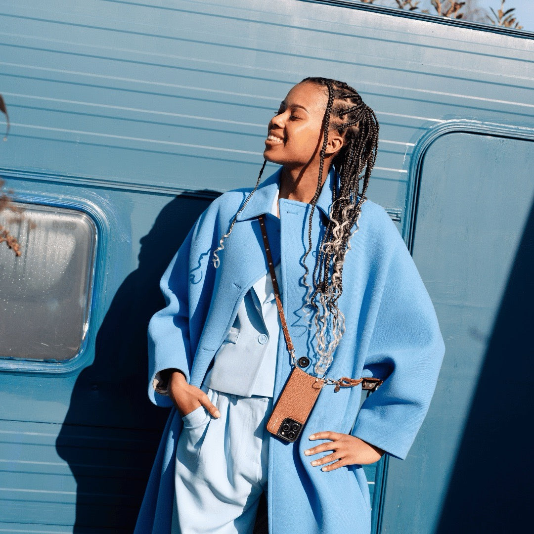 Phone Strap | Slimline Studs | Brown showcased with a stylish outfit against a blue backdrop.