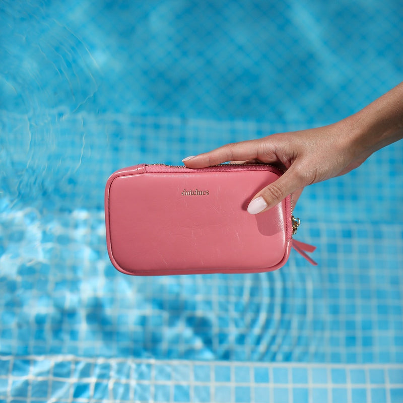 Hand holding a stylish Phone Bag Rose | Pink by Dutchies above a blue pool water.