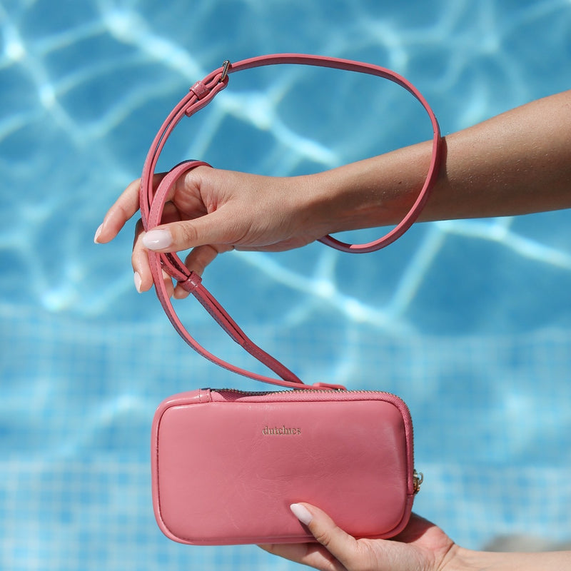 Phone Bag Rose Set | Pink held by a person with a pink strap against a swimming pool background.