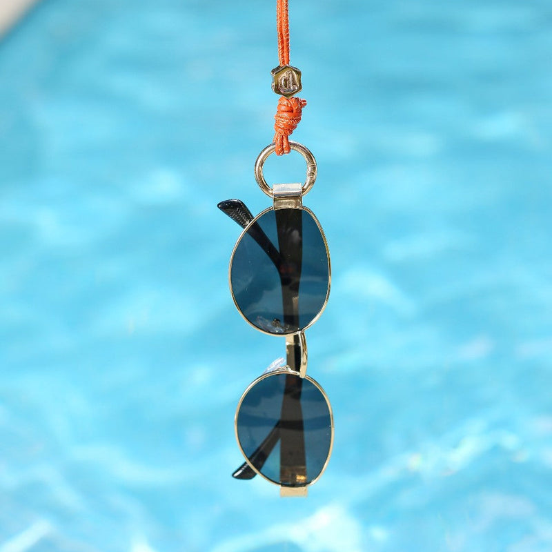 Sunglass Strap | Orange holding stylish sunglasses above a blue pool, combining style and practicality.
