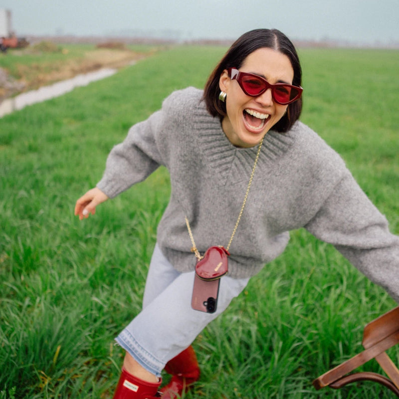 Woman in trendy outfit with Phone Chain | Spanish | Mauve, laughing in a green field, showcasing modern fashion.