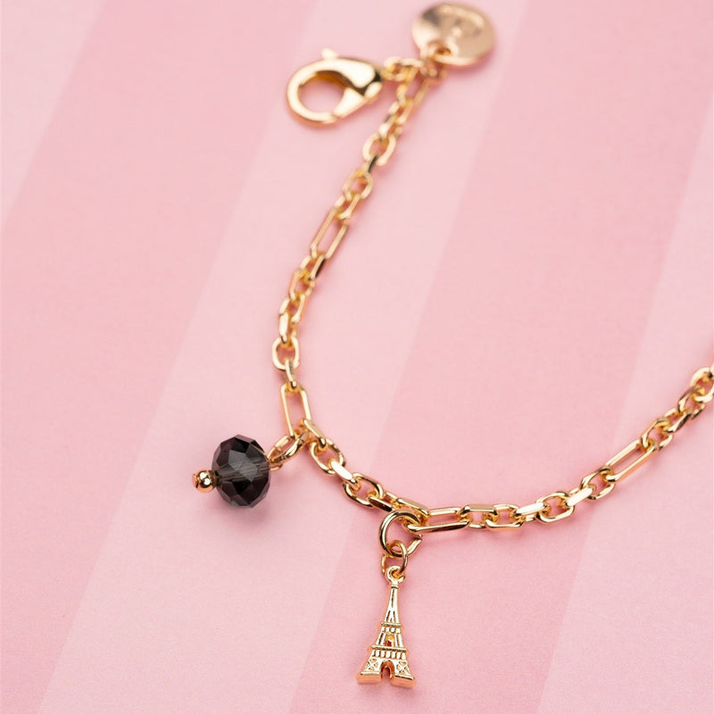 Phone Charm | Gold | Dutch Bandolier featuring Eiffel Tower charm and black bead on a pink background.