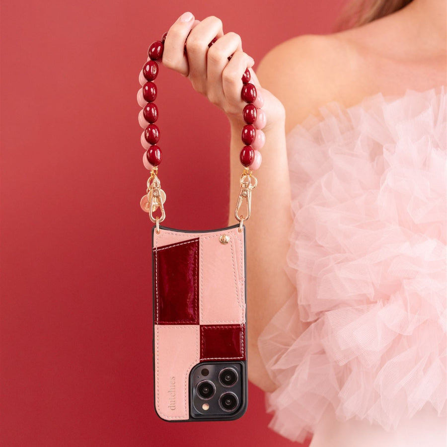 A person holding a mobile phone case with a glossy lollipop color pattern, featuring a cardholder and a chain strap.